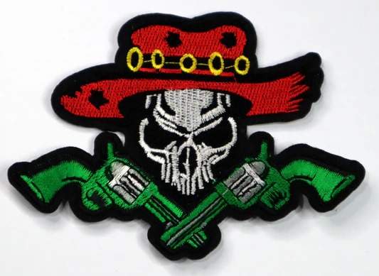 An embroidered patch featuring a skull wearing a red cowboy hat, with two green revolvers crossed below it.
